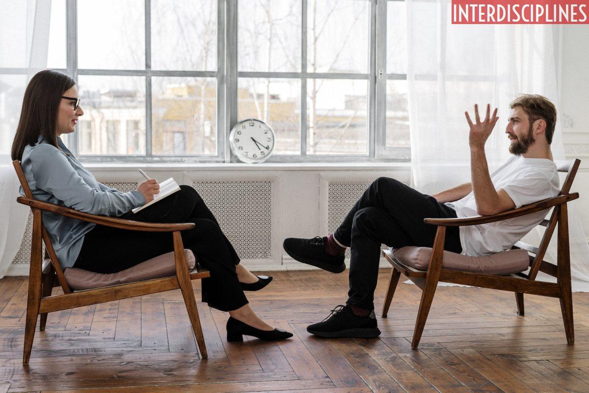 Person in Black Pants and Black Shoes Sitting on Brown Wooden Chair