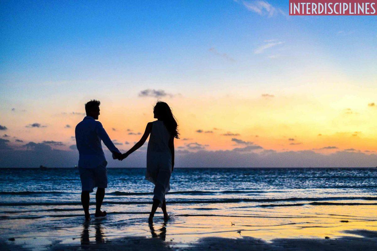 Man and Woman Holding Hands Walking on Seashore during Sunrise