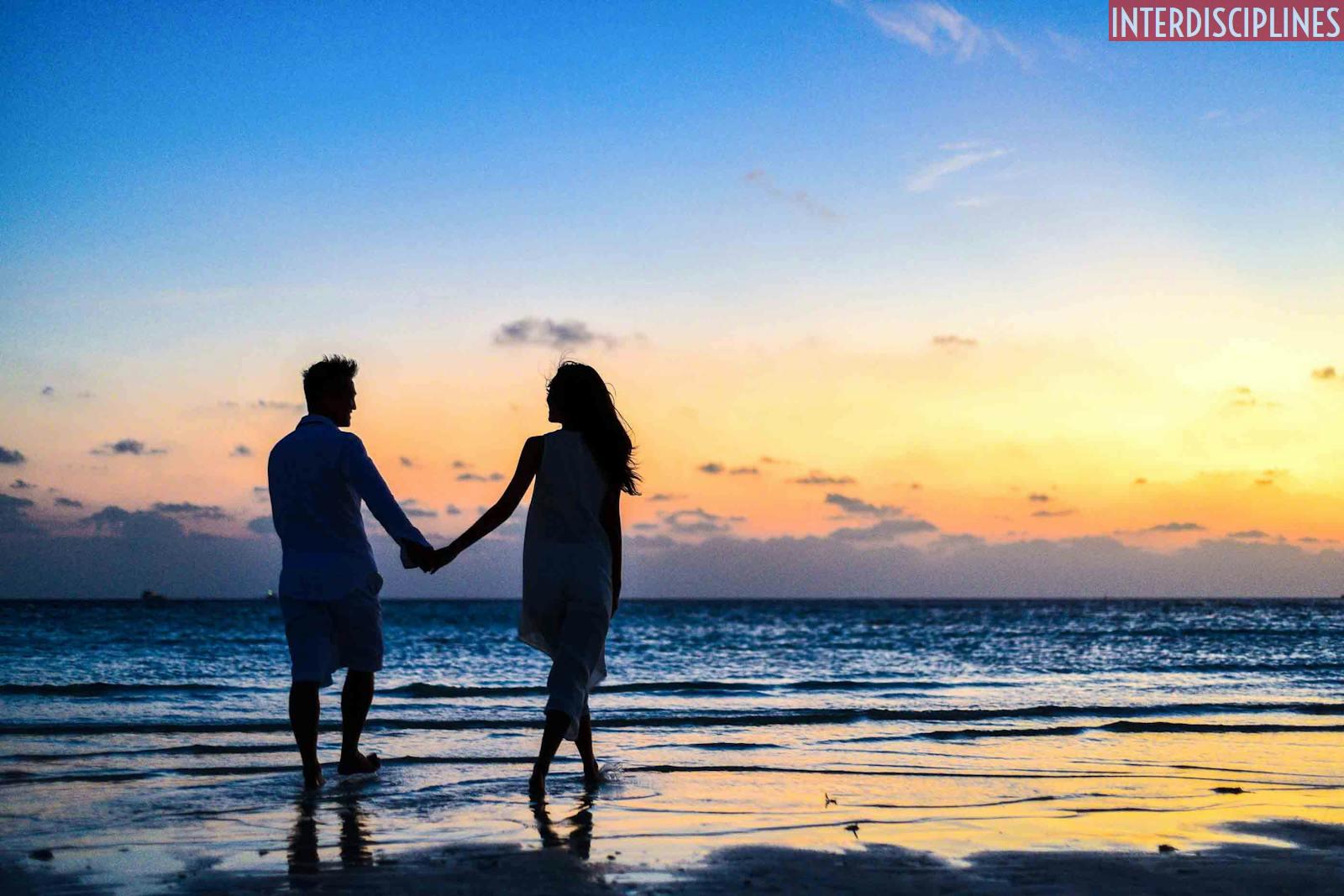 Man and Woman Holding Hands Walking on Seashore during Sunrise