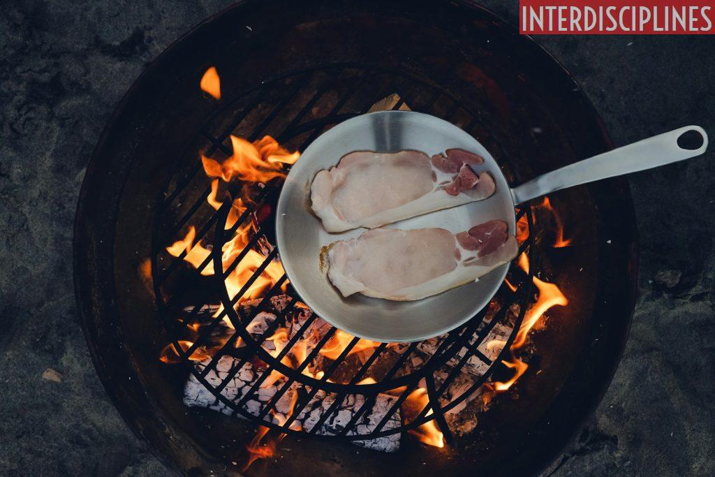 person cooking steak on charcoal gril