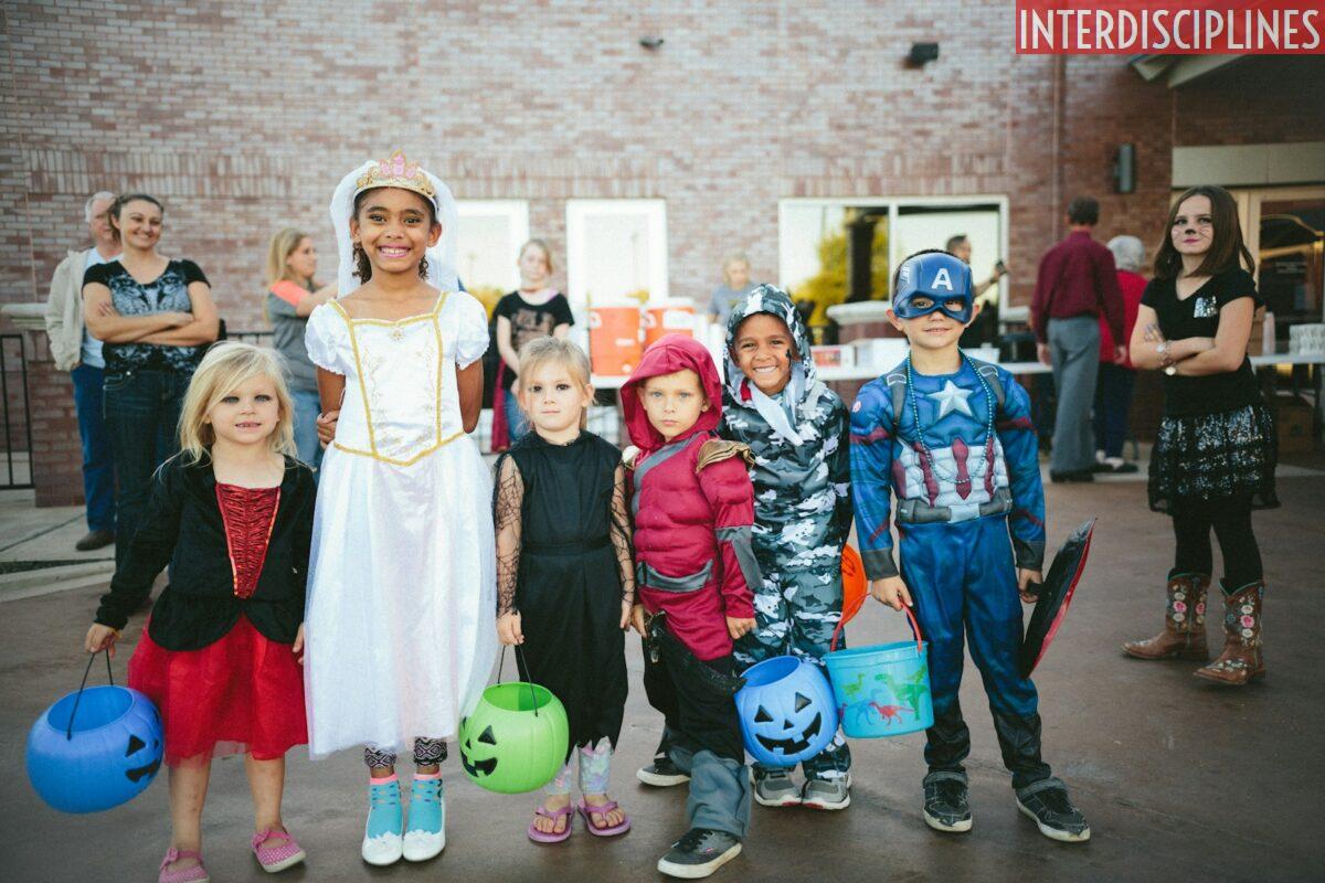 children standing while holding Jack 'o lantern and wearing costume