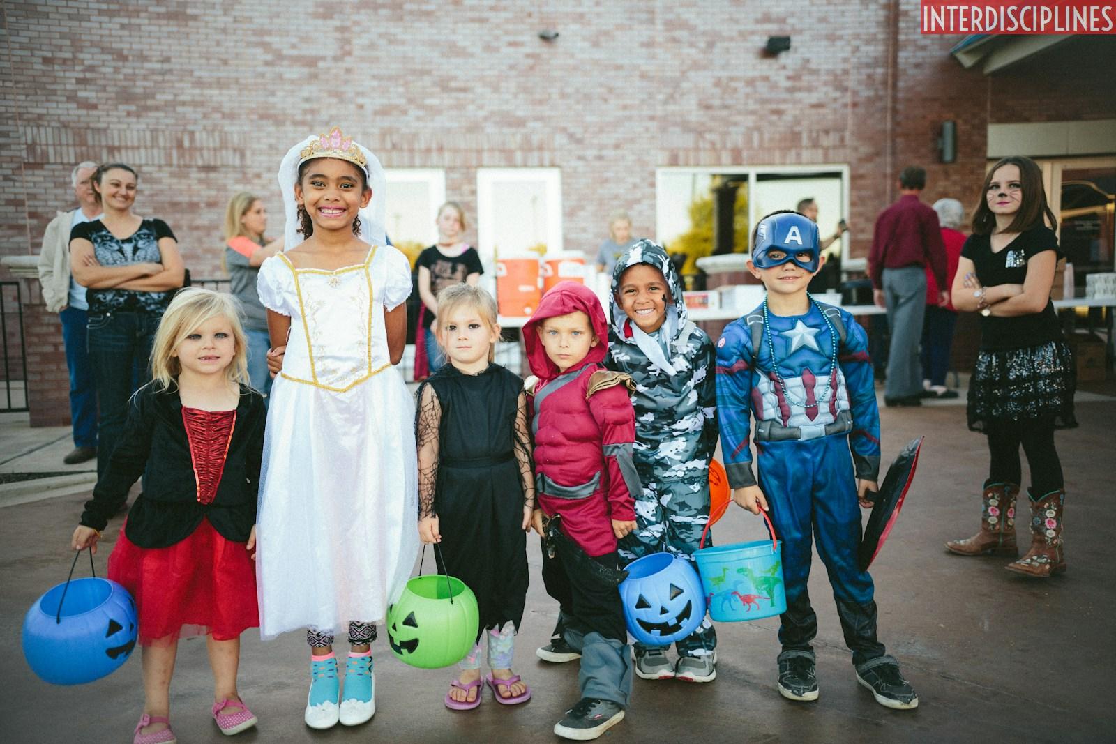 children standing while holding Jack 'o lantern and wearing costume